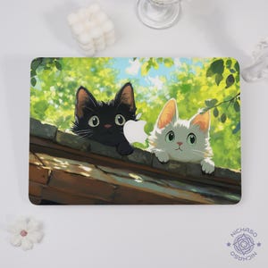 Pode incluir: Uma capa retangular para laptop com uma ilustração de desenho animado de dois gatos espreitando por cima de um telhado. Um gato é preto, o outro branco. O fundo mostra folhagem verde e um céu azul. A capa tem um acabamento brilhante.