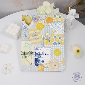 May include: A decorative notebook with a collage of watercolor illustrations. The design includes lemons, a sun, a hat, and the text "La Dolce Vita". The color palette features yellow, blue, and white.