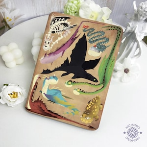 May include: A rectangular, tan-colored case featuring various dragon illustrations in black, purple, green, blue, and yellow. The case has a decorative border and a logo in the bottom right corner. The dragons are in different poses and styles.