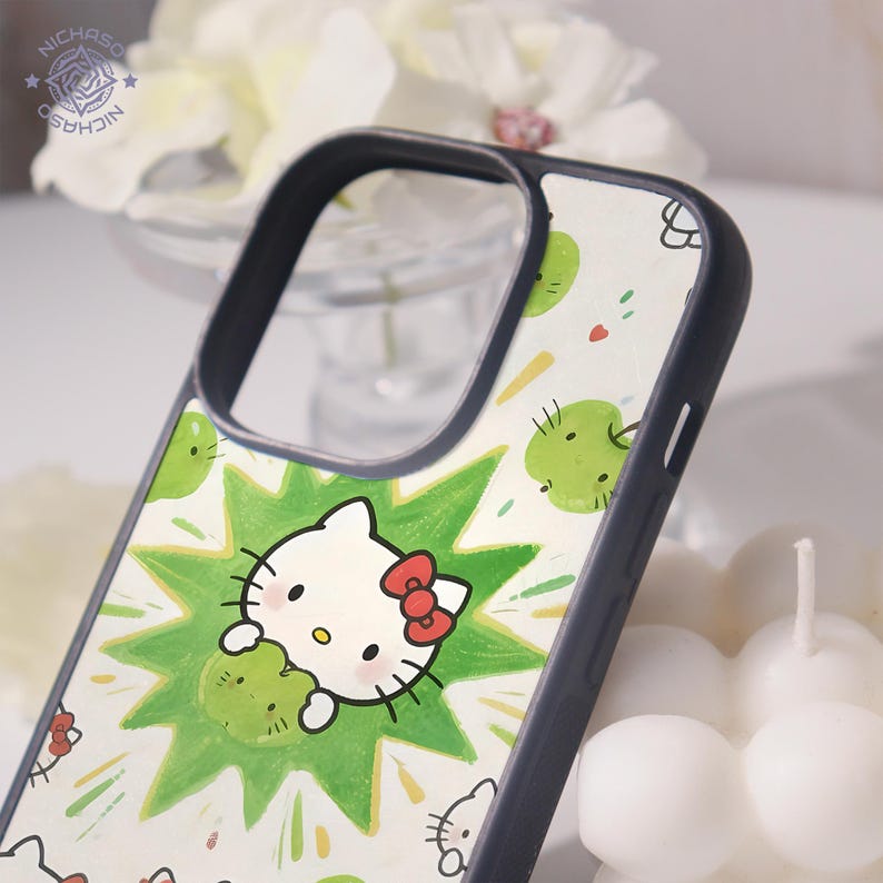 Puede incluir: Funda de tel&eacute;fono con un dise&ntilde;o de Hello Kitty blanco con un lazo rojo, sosteniendo un objeto verde, sobre un fondo blanco con acentos verdes. La funda tiene un borde gris oscuro.