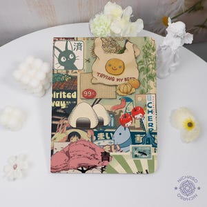 May include: A colorful notebook with a collage of Japanese-inspired illustrations. The design includes a cartoon cat, onigiri, cherries, and the text "Trying My Best". The color palette features pastel tones with a vintage aesthetic.