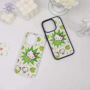 Puede incluir: Dos fundas para tel&eacute;fono sobre un fondo blanco. Las fundas presentan un patr&oacute;n repetido de manzanas verdes y personajes de Hello Kitty. Cada funda tiene un borde negro y un recorte para la c&aacute;mara. Una funda tiene un borde blanco.