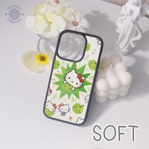 Puede incluir: Funda de tel&eacute;fono con fondo blanco adornada con manzanas verdes y motivos de Hello Kitty. El dise&ntilde;o central muestra a Hello Kitty con un lazo rojo. La funda tiene un borde negro. La palabra "SOFT" es visible.