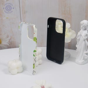 Puede incluir: Dos fundas para tel&eacute;fono. Una es negra, la otra blanca con un estampado verde y amarillo. La funda blanca tiene un dise&ntilde;o de animales de dibujos animados. Las fundas est&aacute;n sobre una superficie blanca.