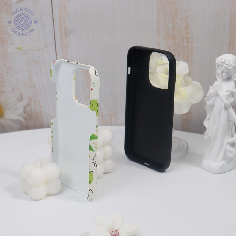 Puede incluir: Dos fundas para tel&eacute;fono. Una es negra, la otra blanca con un estampado verde y amarillo. La funda blanca tiene un dise&ntilde;o de animales de dibujos animados. Las fundas est&aacute;n sobre una superficie blanca.