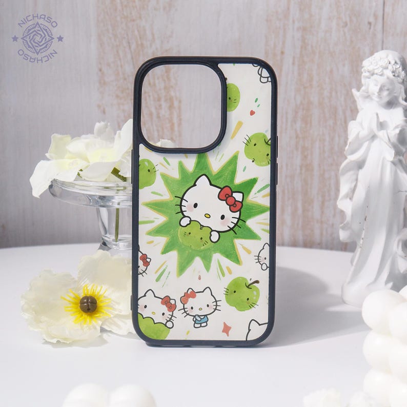 Puede incluir: Funda de tel&eacute;fono con fondo blanco y borde negro. Presenta un dise&ntilde;o de dibujos animados de Hello Kitty, manzanas verdes y un dise&ntilde;o de estrella verde. La funda tiene un recorte para la c&aacute;mara.