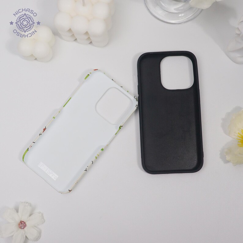Puede incluir: Dos fundas para tel&eacute;fono, una negra y otra blanca con un dise&ntilde;o floral, se muestran sobre una superficie blanca. La funda negra es lisa, mientras que la blanca tiene un patr&oacute;n colorido en los bordes. Las fundas est&aacute;n dise&ntilde;adas para un smartphone.