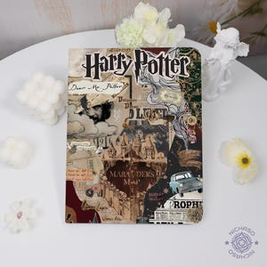 May include: A hardcover notebook with a collage design featuring the text "Harry Potter." The design includes images of Hogwarts, the Marauder's Map, and other elements from the series. The notebook is on a white surface.