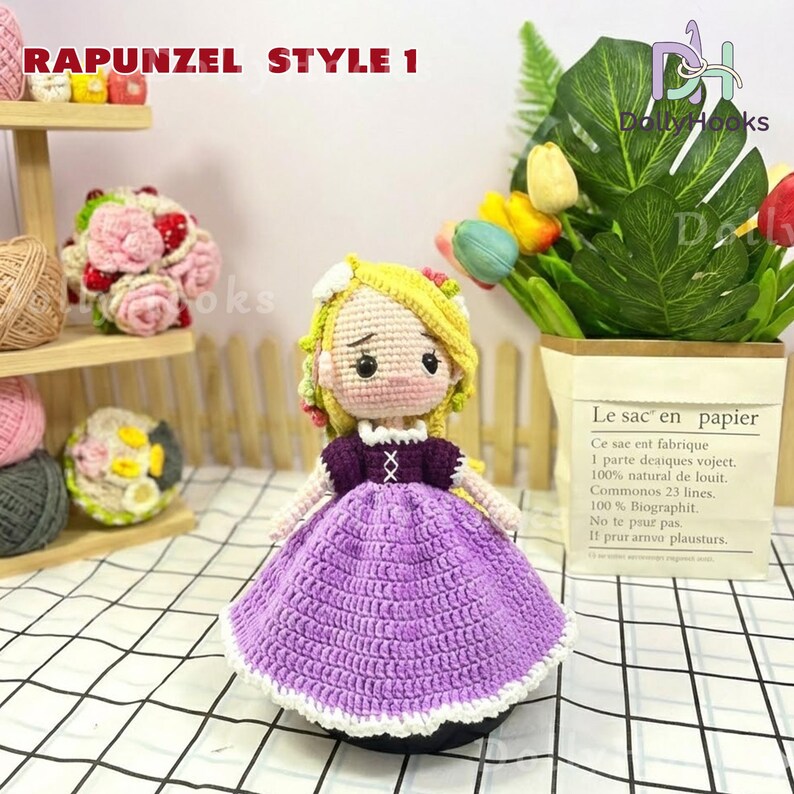 May include: A handmade crochet doll in the style of Rapunzel, featuring a yellow yarn hair, a purple dress, and a white collar. The doll is displayed with other handmade items and a paper bag with text.