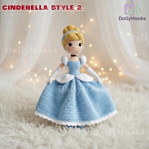May include: Crocheted Cinderella doll in a light blue ball gown with white accents. The doll has blonde hair styled in a bun with a blue headband, and is wearing white gloves. The text "CINDERELLA STYLE 2" is at the top.