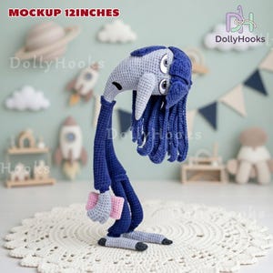 May include: A handmade crochet doll, approximately 12 inches tall, in shades of blue, gray, and pink. The doll has a long neck, a head with large eyes, and long blue hair. It is standing on a white, lacy surface.