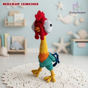 Puede incluir: Un juguete de gallo de ganchillo hecho a mano, de aproximadamente 30 cm de altura, con cresta roja, cuello amarillo y cuerpo azul y verde. El gallo tiene ojos grandes y est&aacute; sobre un tapete circular blanco. El texto "MOCKUP 12 INCHES" es visible.