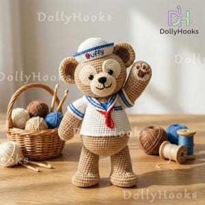 May include: A handmade crochet bear wearing a sailor outfit. The bear is tan with a white and blue sailor shirt, a white hat with "Duffy" on it, and a red necktie. A basket of yarn and crochet hooks are in the background.
