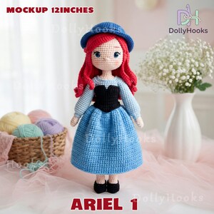 Puede incluir: Mu&ntilde;eca de ganchillo hecha a mano de un personaje con cabello rojo, que lleva un vestido azul, un top negro y un sombrero azul. La mu&ntilde;eca mide aproximadamente 30 cm de altura. El texto "ARIEL 1" est&aacute; en la parte inferior de la imagen.