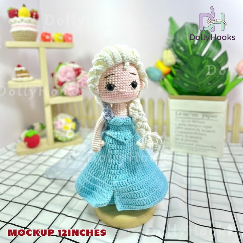 May include: A handmade crochet doll of a character with blonde hair in a braid, wearing a light blue dress. The doll is approximately 12 inches tall. The doll is displayed on a light-colored base.