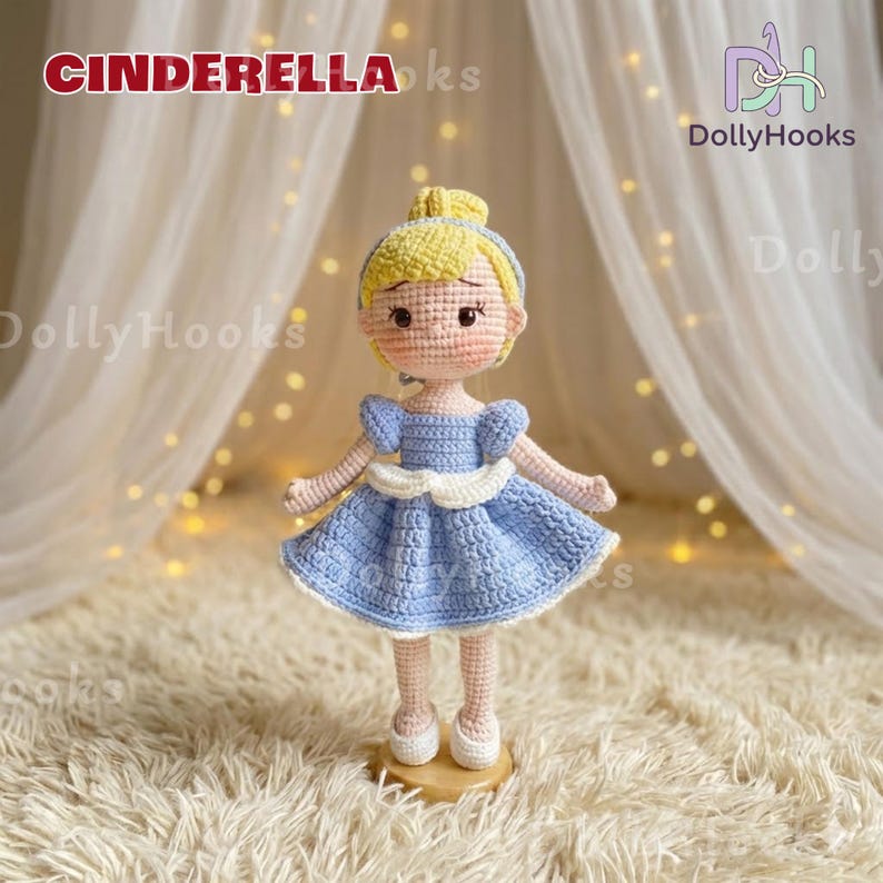 May include: A handmade crochet doll of Cinderella, wearing a light blue dress with a white trim. The doll has blonde hair and is standing on a wooden base. The text "CINDERELLA" is at the top of the image.