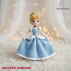 Op de afbeelding: Een handgemaakte gehaakte pop van Assepoester, gekleed in een lichtblauwe jurk met witte accenten. De pop heeft blond haar en is ongeveer 35.5 cm hoog. De tekst "DollyHooks" en "MOCKUP 14 INCHES" zijn zichtbaar.