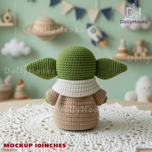 May include: A green crochet doll with large pointed ears, wearing a tan robe and a white collar. The doll is 10 inches tall as indicated by the text. It is positioned on a white circular lace doily. The doll has a rounded head and arms.