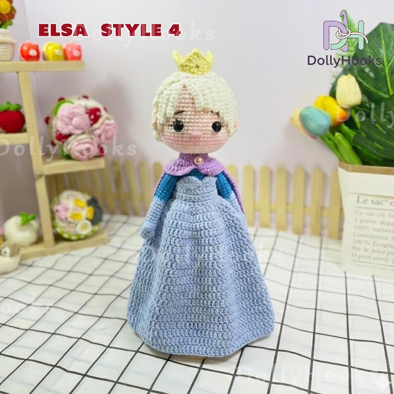 May include: Crocheted doll in the style of Elsa, featuring a light blue dress, a purple cape, and a golden crown. The doll has blonde hair and a pink face. The text "ELSA STYLE 4" is visible in the image.