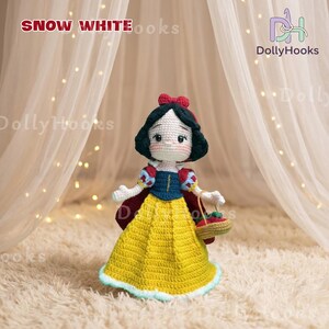 May include: A handmade crochet doll of Snow White, featuring a yellow dress, red cape, and a basket of apples. The doll has black hair, a red bow, and is holding a small basket. The text "Snow White" is at the top.