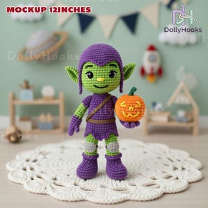 May include: A handmade crochet goblin doll, approximately 12 inches tall, holding an orange pumpkin. The goblin is green and purple, with a smiling face and pointed ears. The pumpkin has a carved jack-o'-lantern face. The doll is on a white, lacy surface.