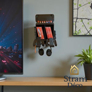 Può includere: Un organizer per console di gioco in metallo nero da parete. È dotato di scomparti per cartucce di gioco e controller, con slot per cuffie. L'organizer è montato su una parete grigia, con una TV e opere d'arte sullo sfondo.