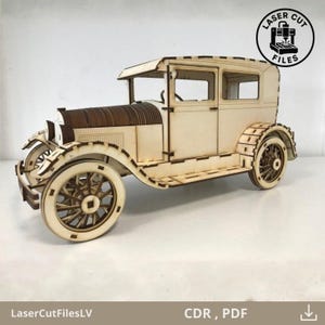 May include: A wooden model of a vintage car, laser-cut from light-colored wood. The car features detailed wheels, a roof, and a distinct front grill. The image includes the text "Laser Cut Files" in a circular logo.