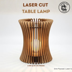 Puede incluir: Una lámpara de mesa cortada con láser hecha de madera contrachapada de 3 mm. La lámpara tiene un diseño único con listones de madera verticales que se curvan hacia adentro. El texto "LASER CUT TABLE LAMP" está en la parte superior. La lámpara está iluminada desde adentro.