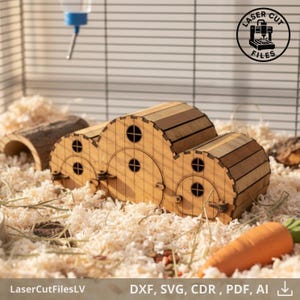Può includere: Casa per criceti in legno con più camere collegate, con finestre e porte rotonde. La casa è realizzata in legno chiaro e si trova in una gabbia con trucioli di legno, un abbeveratoio e una carota.