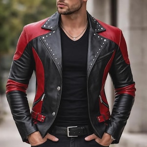 Op de afbeelding: Een zwart en rood leren jack met zilveren studs op de kraag en schouders. De jas heeft een klassieke biker-stijl met een revers, ritssluitingen en een gespriem. De mouwen hebben rode accenten.