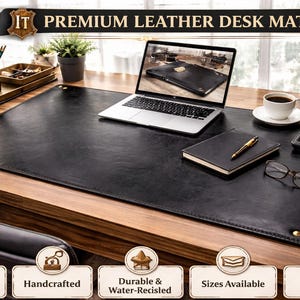 Puede incluir: Una alfombrilla de escritorio de cuero negro de primera calidad con un portátil, un cuaderno y accesorios. La alfombrilla de escritorio es rectangular y cubre la mayor parte del escritorio de madera. El texto "IT PREMIUM LEATHER DESK MAT" está en la parte superior.