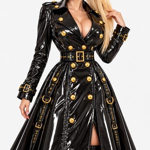 Peut inclure: Un trench-coat en cuir verni noir doté d'un devant croisé avec des boutons dorés, d'une ceinture assortie à boucle, et de sangles à boucles sur les poignets et les pans de la jupe. Le manteau présente un large col et une coupe évasée.