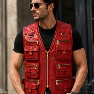 May include: A red leather utility waistcoat featuring a central gold-tone zip, multiple front pockets with gold zips and snap-button flaps, and integrated D-rings on the chest. The sleeveless garment has a structured design with side straps.