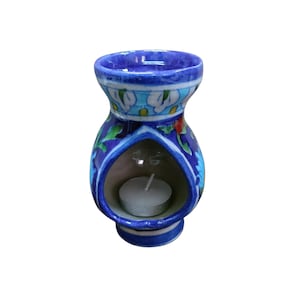 Puede incluir: Difusor de aceites esenciales de cerámica azul con motivos florales y una vela de té en su interior. El difusor tiene una base redonda, una abertura central y una abertura superior. El diseño floral incluye flores blancas y azules con hojas verdes.