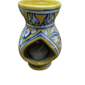 Puede incluir: Un difusor de aceites esenciales de cerámica amarilla con diseños florales azules y blancos. El difusor tiene una abertura en forma de corazón para sostener una vela de té. El diseño incluye una base, una sección media y una abertura superior.