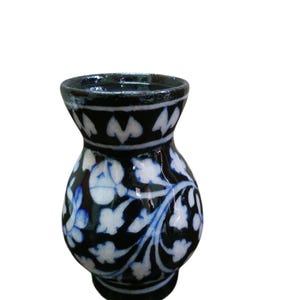 May include: A small ceramic vase with a black base and a flared rim. The vase has a detailed floral pattern in white and blue against a black background. The rim has a white and black geometric design.