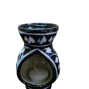 Puede incluir: Un difusor de aceites esenciales de cerámica con esmalte azul oscuro y patrones florales blancos. El difusor tiene una abertura en forma de corazón para sostener una vela de té. El diseño incluye una base pequeña y una parte superior acampanada.