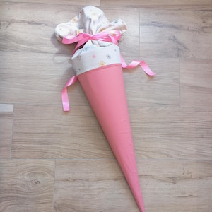 May include: A cone-shaped school gift bag featuring a solid pink lower section and a white upper fabric cuff decorated with small, colorful dandelion-like patterns. The top is gathered and secured with a bright pink satin ribbon tied in a bow.
