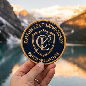 Peut inclure: Un écusson brodé bleu marine de forme circulaire avec une bordure dorée. Le centre présente un écusson doré contenant les lettres CL et une aiguille. Le texte CUSTOM LOGO EMBROIDERY PATCH SPECIALISTS est brodé en doré autour de l'écusson.