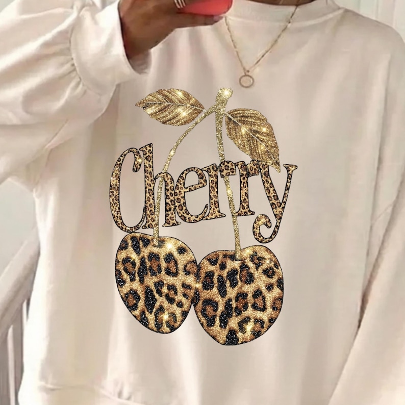 Puede incluir: Sudadera color crema con un dise&ntilde;o de cereza con estampado de leopardo brillante. La palabra "Cherry" est&aacute; escrita encima de las cerezas en un estampado de leopardo a juego. La sudadera tiene mangas largas y cuello redondo.