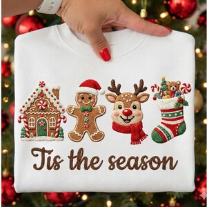 May include: White sweatshirt with embroidered Christmas designs, including a gingerbread house, gingerbread man, reindeer, and stocking. The text "Tis the season" is embroidered below the designs.