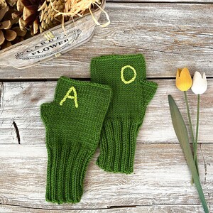 May include: A pair of green knitted fingerless gloves with yellow letters, one glove says "A" and the other says "O".