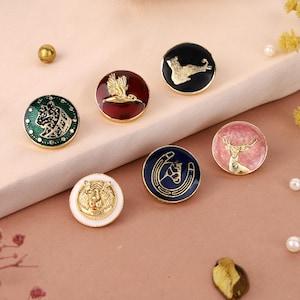 May include: A collection of decorative round buttons with various animal and symbol designs. The buttons feature gold, white, black, red, green, and pink enamel backgrounds. Designs include a tiger, a horse, a deer, a bird, a seal, and a horseshoe.
