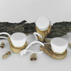 Può includere: Tre spazzole per il viso in legno con setole bianche e finiture dorate. Ogni spazzola ha un manico in legno unico ed è collegata a una corda bianca. Le spazzole sono disposte su una superficie bianca con trucioli di legno e un pezzo di corteccia.