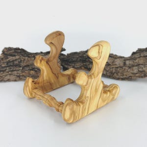 Könnte beinhalten: Handgefertigter Telefonständer aus Olivenholz. Der Ständer hat ein einzigartiges, geschwungenes Design und ein natürliches Holzmaserungsmuster. Er ist etwa 15 cm lang und 10 cm breit. Helles Holz.