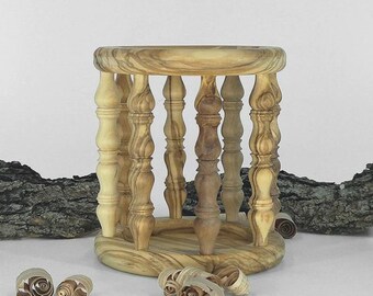 May include: A handcrafted wooden decorative holder with a round top and base, connected by vertical spindles. The holder is made of light-colored wood with a natural grain pattern. Wood shavings are scattered around the base. The overall design is rustic and elegant.