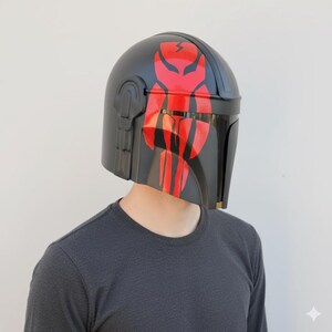 May include: A black helmet with a red and black design. The helmet has a visor and is likely a costume piece or prop. The design features a red emblem on the top and red stripes on the front.