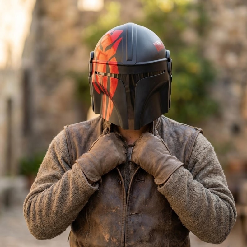 May include: A black and red helmet with a distinctive design, worn with a brown leather jacket and gloves. The helmet features red markings and a visor. The person is wearing a brown jacket and gloves.
