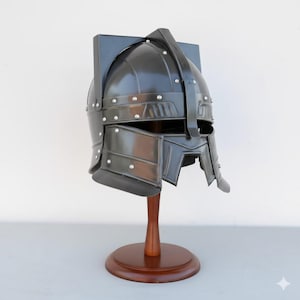 Peut inclure: Casque en métal noir avec des rivets, présenté sur un support en bois. Le casque est doté d'une visière et d'une crête, évoquant une esthétique médiévale ou fantastique. Le support a une base ronde et une tige fine.