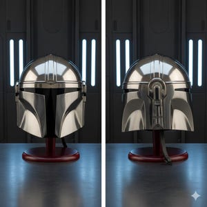 Op de afbeelding: Twee gepolijste zilveren Mandalorian helmen worden gepresenteerd op rode standaards. De helmen hebben een strakke, metalen afwerking met kenmerkende vizier vormen en ingewikkelde details. De achtergrond is donkergrijs met verticale witte lichten.